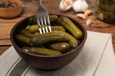 Eating tasty pickled cucumbers with fork at wooden table