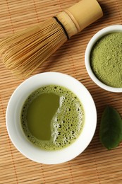 Photo of Cup of fresh matcha tea, green powder and chasen on bamboo mat, flat lay