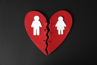 Photo of Halves of cut felt heart with paper man and woman pinned together on black background, top view
