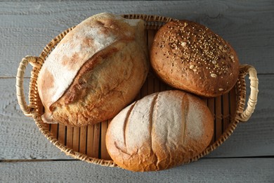 Photo of Wicker basket with different types of fresh bread on grey wooden table, top view