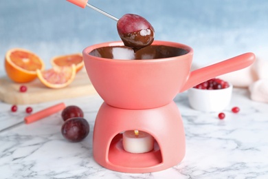 Photo of Dipping grape into pot with chocolate fondue on table