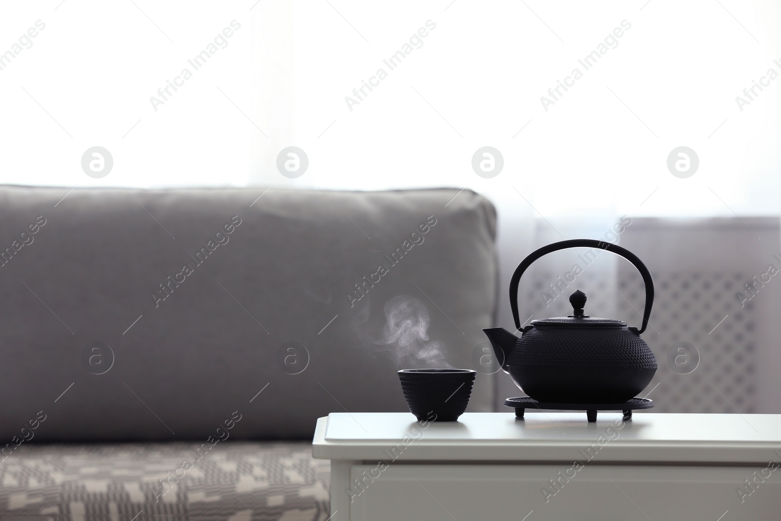 Photo of Teapot and cup of fresh hot tea on white table against blurred background. Space for text