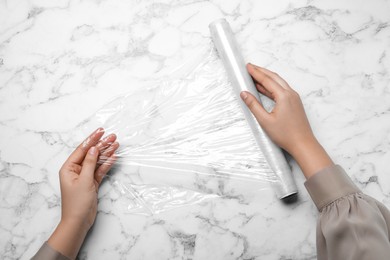 Photo of Woman with roll of stretch wrap at white marble table, top view