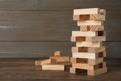 Photo of Jenga tower made of wooden blocks on table, space for text