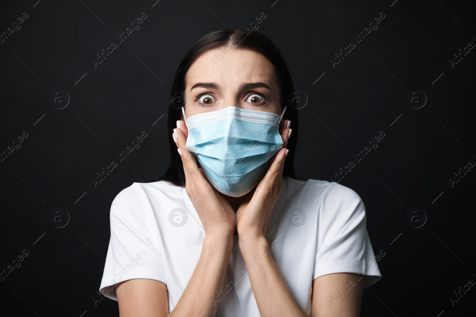 Photo of Young woman with protective mask feeling fear on black background