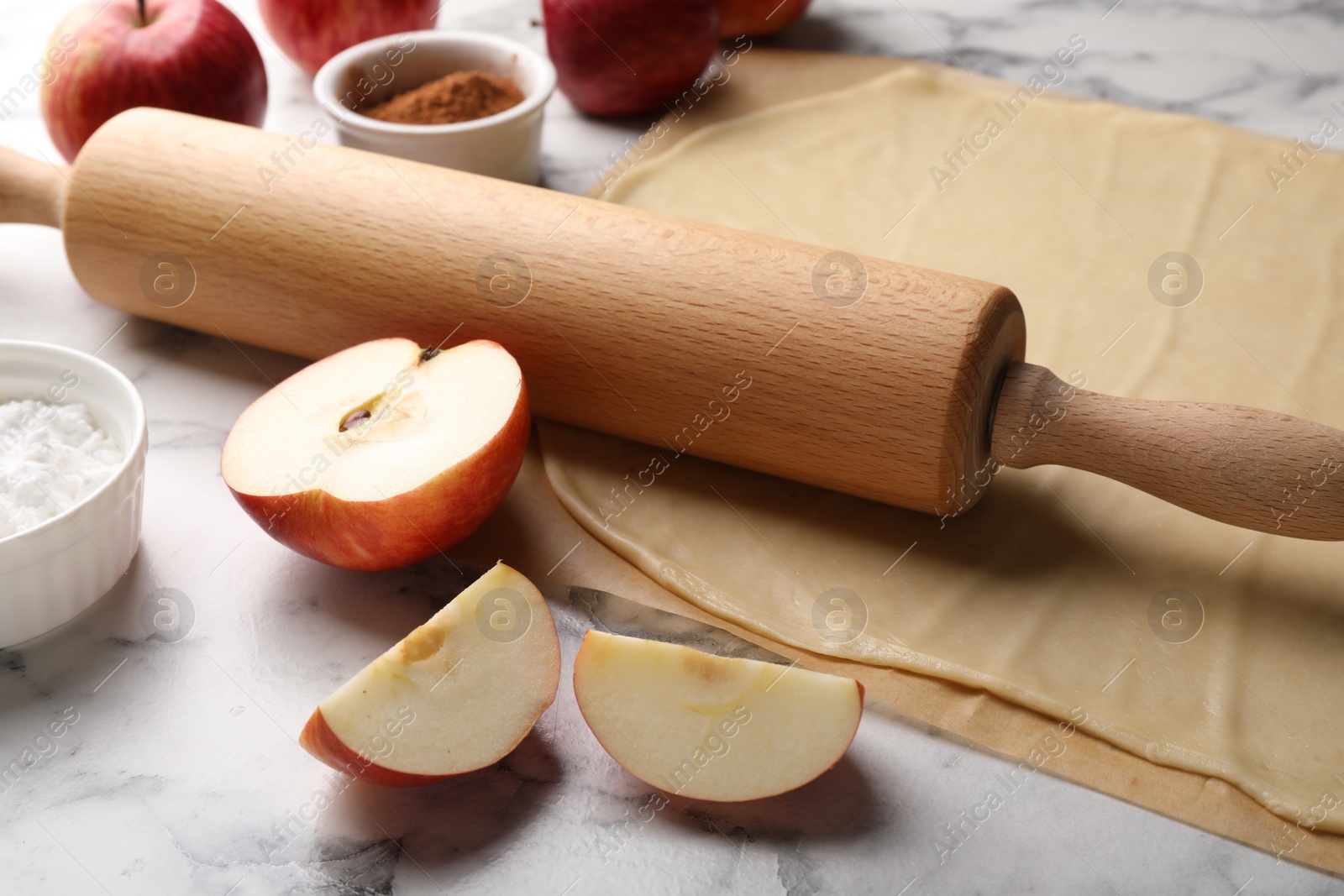 Photo of Fresh dough, rolling pin and ingredients on white marble table, closeup. Making apple pie