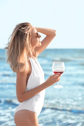 Photo of Young woman with glass of wine on beach