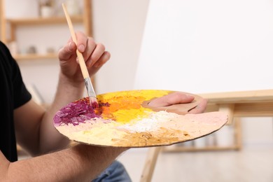 Photo of Man with brush and artist`s palette painting in studio, closeup. Using easel to hold canvas