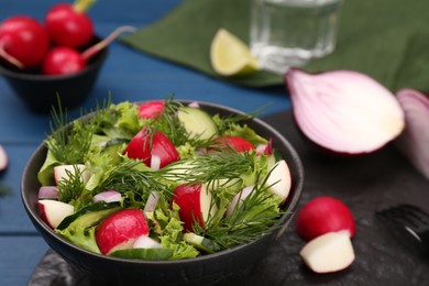 Photo of Tasty salad with radish in bowl on blue table, closeup