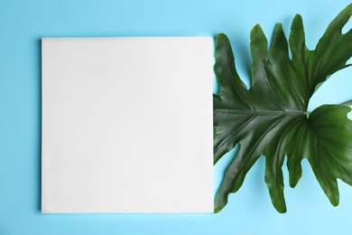 Blank card with tropical leaf on color background, top view