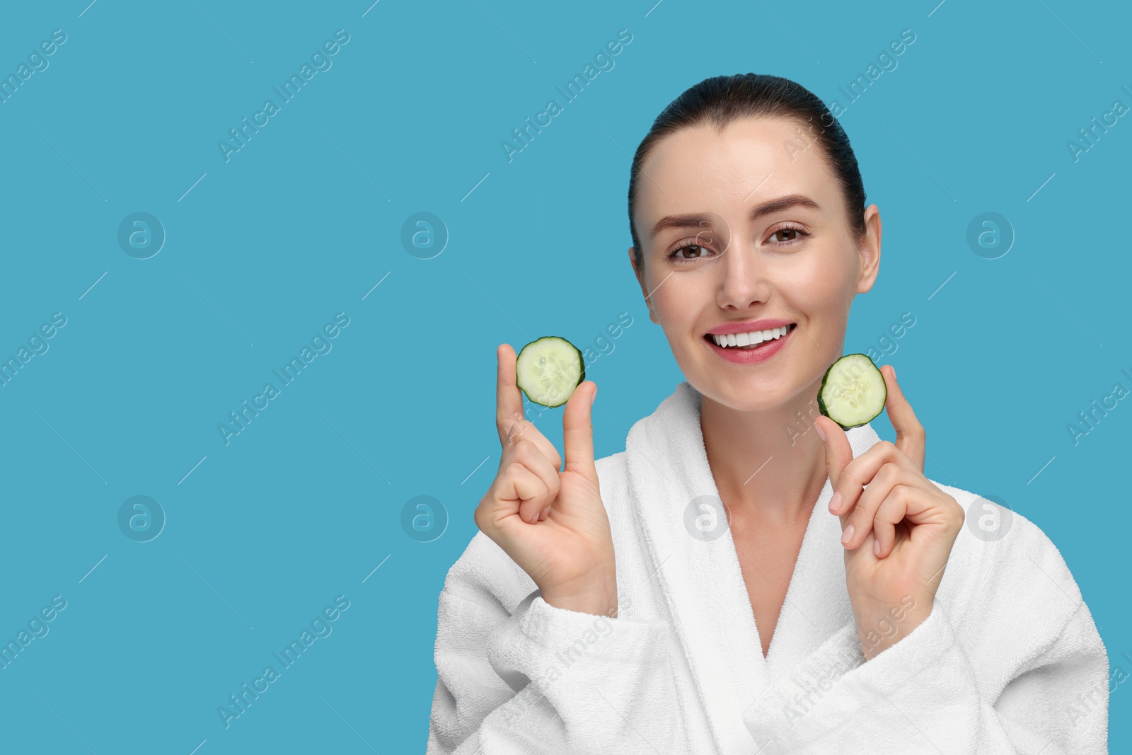 Photo of Beautiful woman with pieces of cucumber on light blue background, space for text