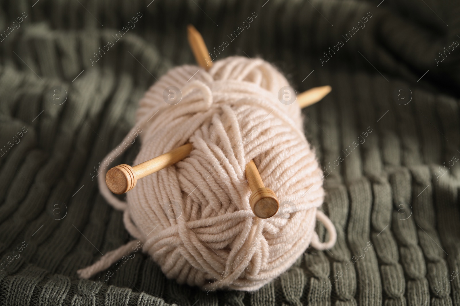 Photo of Beige woolen yarn and needles on green knitted fabric, closeup