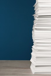 Photo of Stack of white paper sheets on wooden table against blue background, space copy text
