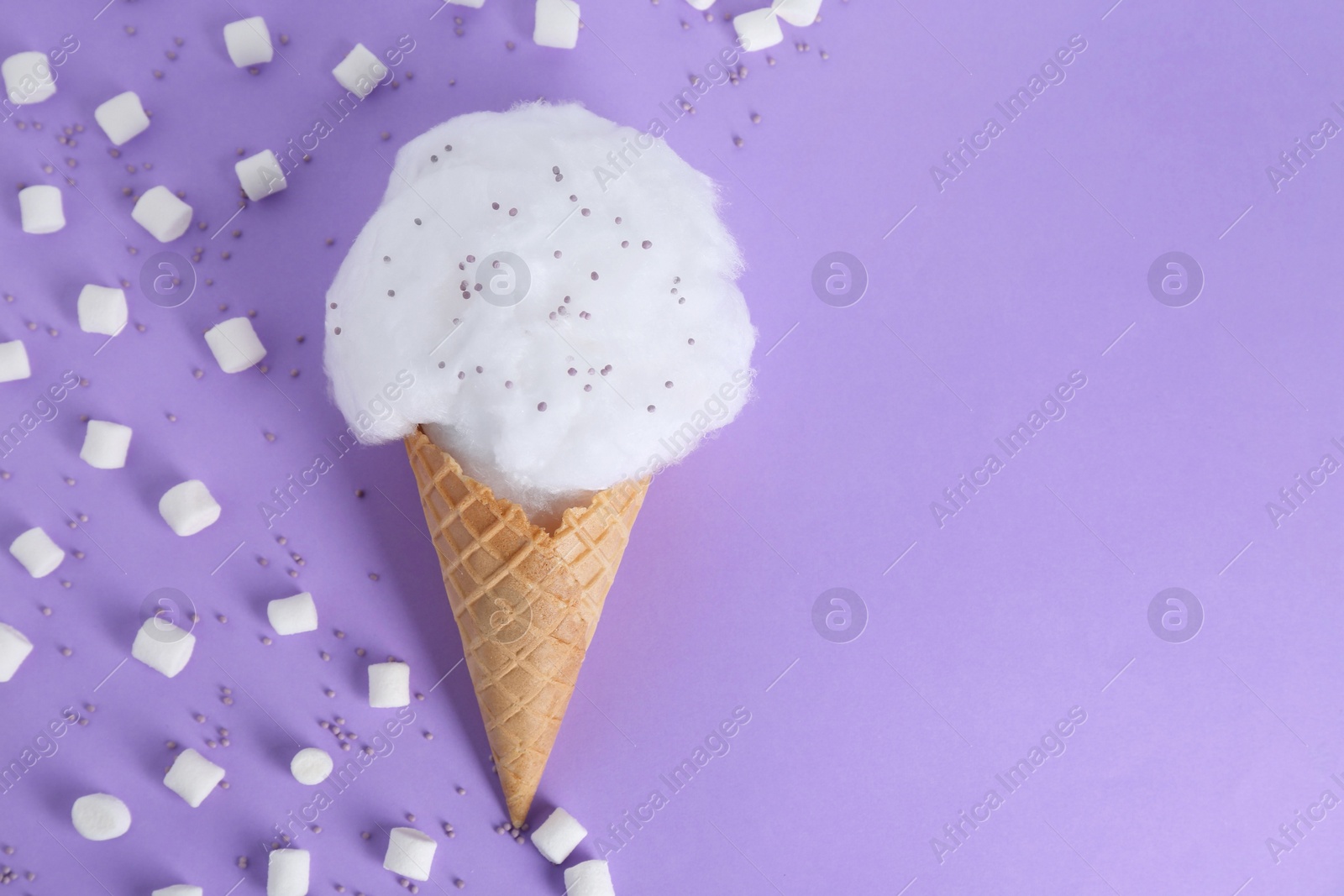 Photo of Sweet cotton candy in waffle cone and marshmallows on purple background, flat lay. Space for text