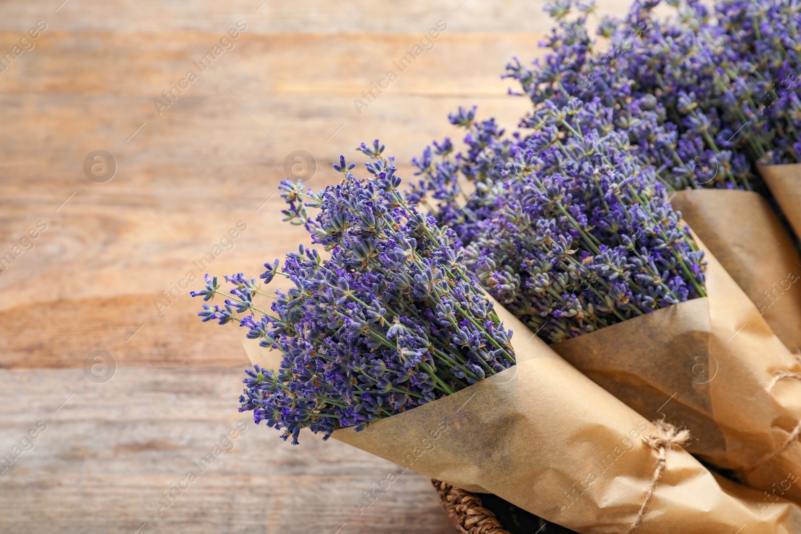 Photo of Fresh lavender flowers in basket on wooden table, closeup. Space for text