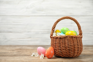 Photo of Colorful Easter eggs in basket and flowers on wooden table. Space for text