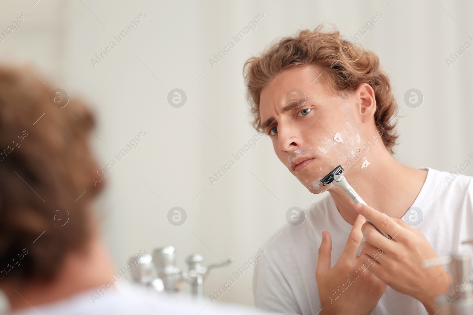 Photo of Young handsome man shaving in bathroom