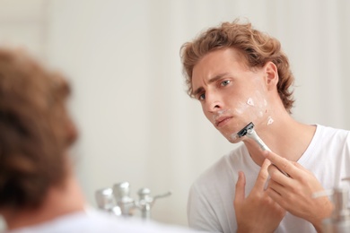 Photo of Young handsome man shaving in bathroom