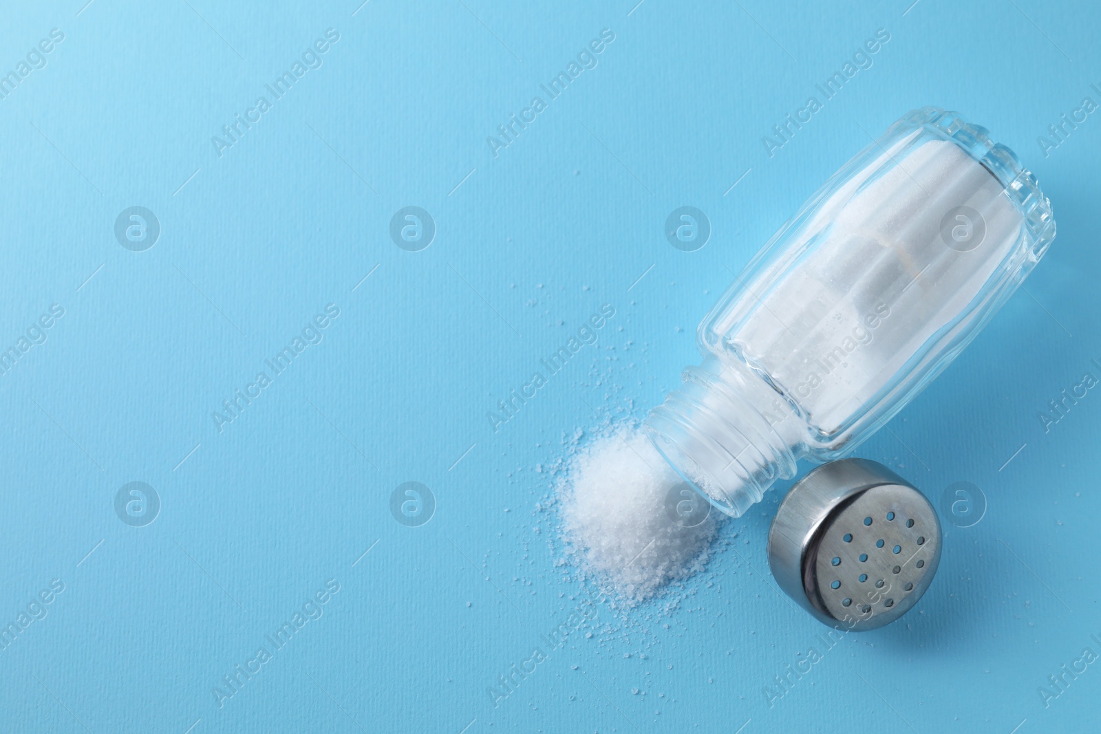 Photo of Organic white salt in shaker on light blue background, top view. Space for text