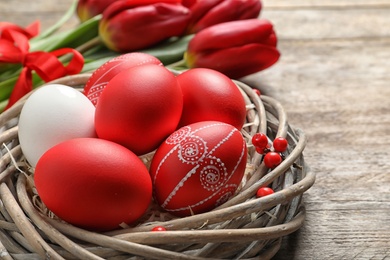 Photo of Wicker nest with painted Easter eggs on table, closeup