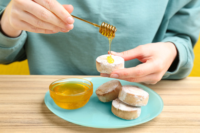 Photo of Woman pouring honey onto cookie at wooden table, closeup