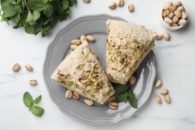 Photo of Pieces of tasty halva with pistachios and mint on white table, flat lay