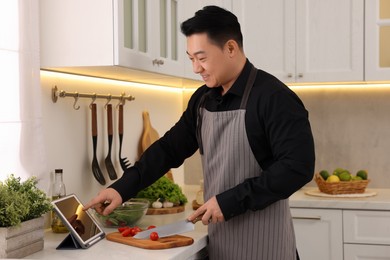 Photo of Man using tablet while cooking in kitchen