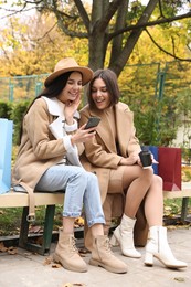 Special Promotion. Happy young women with smartphone and shopping bags in park