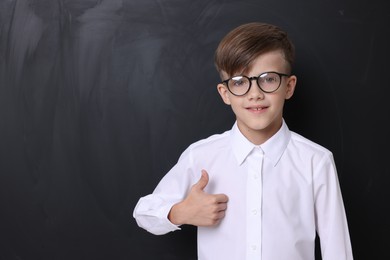 Photo of Cute schoolboy in glasses showing thumbs up near chalkboard, space for text