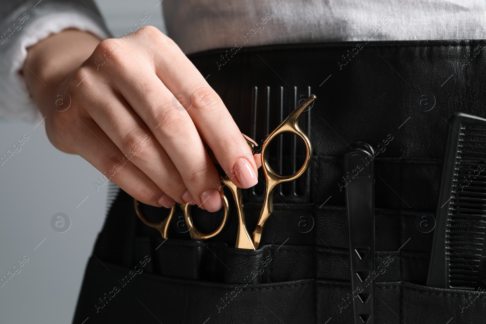 Photo of Hairstylist with professional tools in waist pouch on grey background, closeup