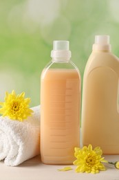 Photo of Bottles of laundry detergents, towel and beautiful flowers on white wooden table