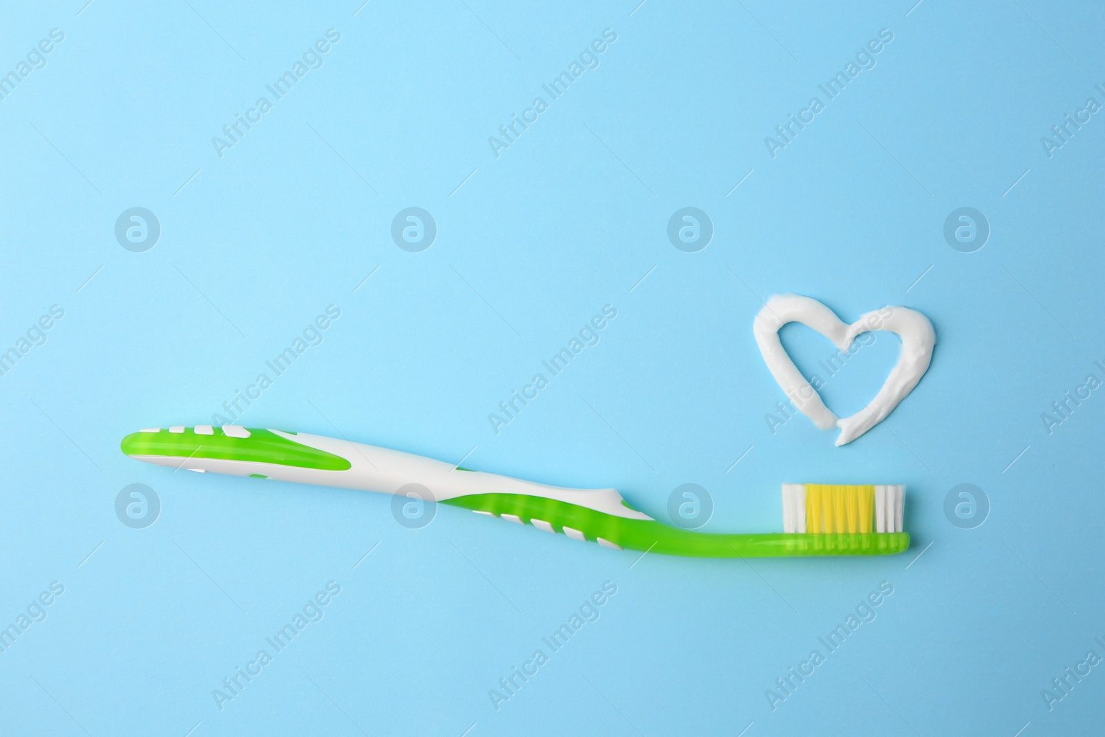 Photo of Heart made with toothpaste and brush on light blue background, top view