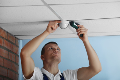 Technician installing CCTV camera on ceiling indoors