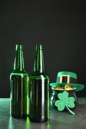 St. Patrick's day celebration. Beer in green bottles, leprechaun hat, pot of gold and decorative clover leaf on grey table. Space for text
