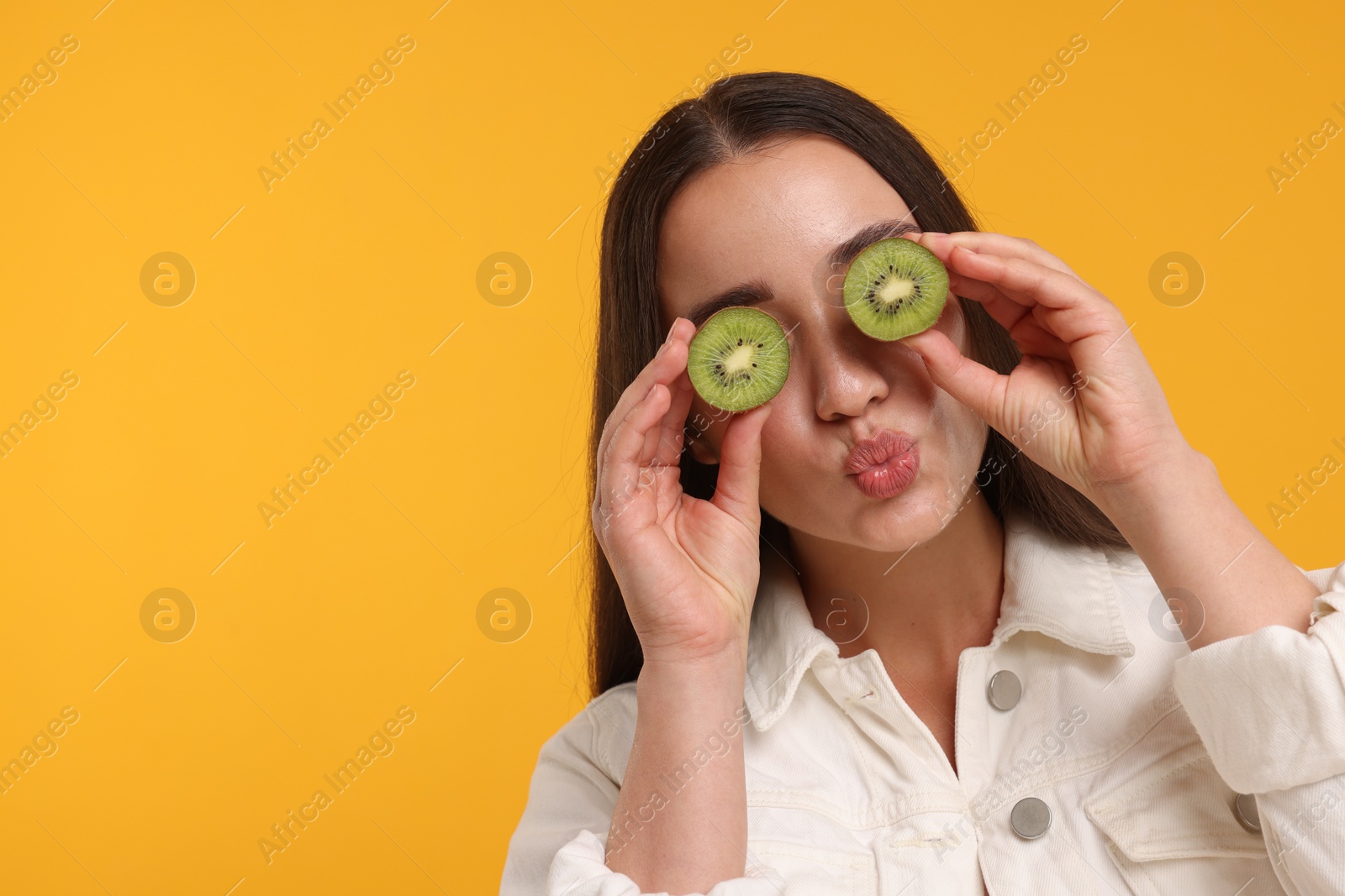 Photo of Woman covering eyes with halves of kiwi on yellow background, space for text