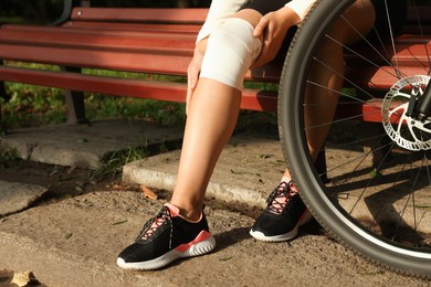 Photo of Woman with injured knee on wooden bench near bicycle outdoors, closeup
