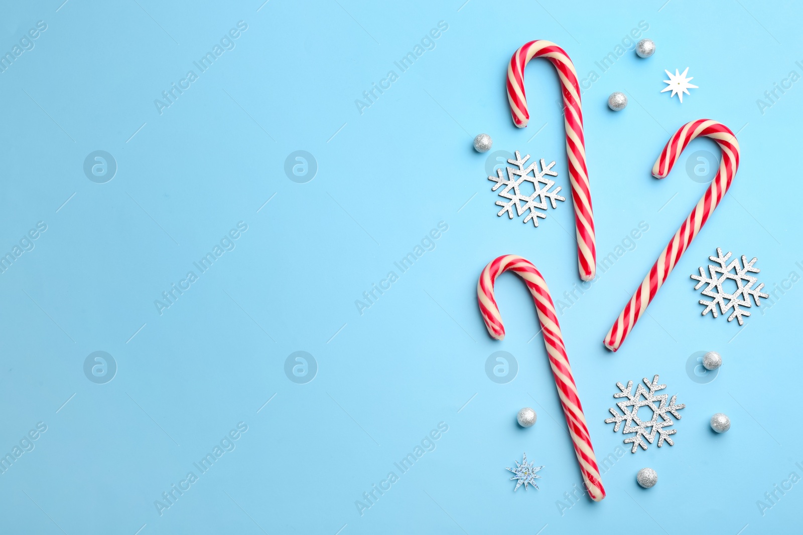 Photo of Candy canes and snowflakes on light blue background, flat lay with space for text. Christmas treat