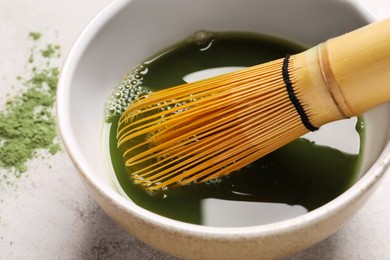 Photo of Bowl of fresh matcha tea with bamboo whisk on light table, closeup