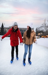 Happy young couple skating at outdoor ice rink