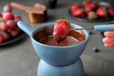 Photo of Woman dipping strawberry into pot with chocolate fondue at table, closeup