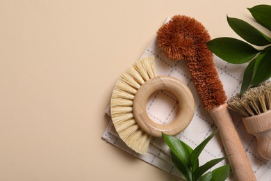 Photo of Cleaning brushes, towel and green leaves on beige background, top view. Space for text