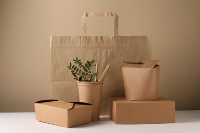 Photo of Eco friendly food packaging. Paper containers, bag, straws and green twigs on white table against beige background