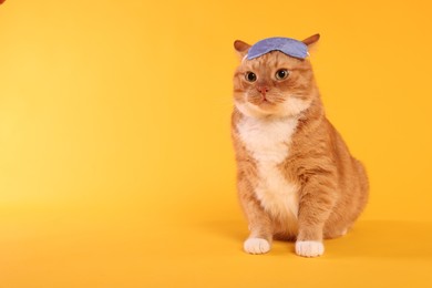 Photo of Cute ginger cat with sleep mask on orange background, space for text