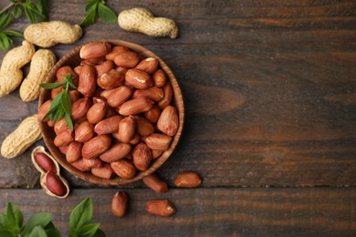 Fresh peanuts and leaves in bowl on wooden table, flat lay. Space for text