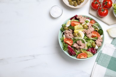 Photo of Bowl of delicious salad with canned tuna and vegetables on white marble table, flat lay. Space for text