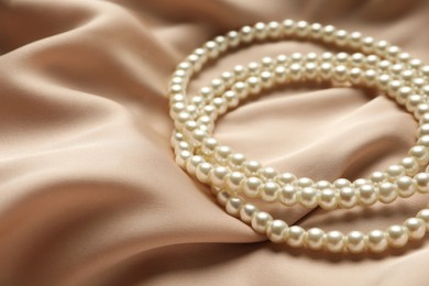 Photo of Elegant necklace with pearls on beige silk, closeup. Space for text