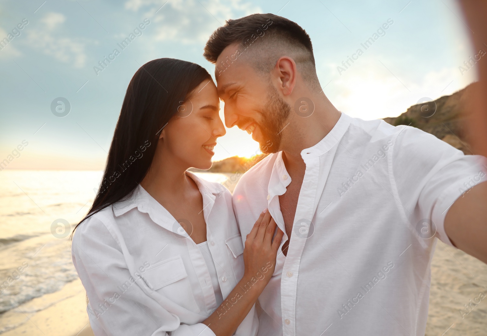 Photo of Happy young couple taking selfie on beach at sunset