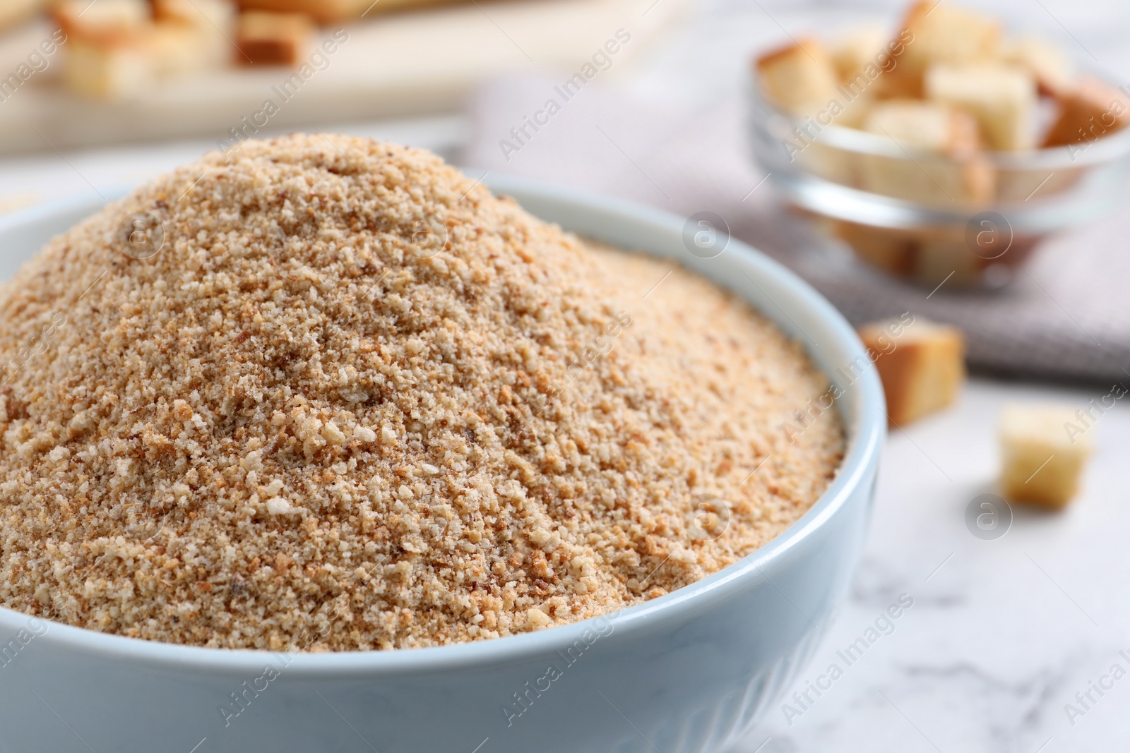 Photo of Fresh breadcrumbs in bowl on white marble table, closeup