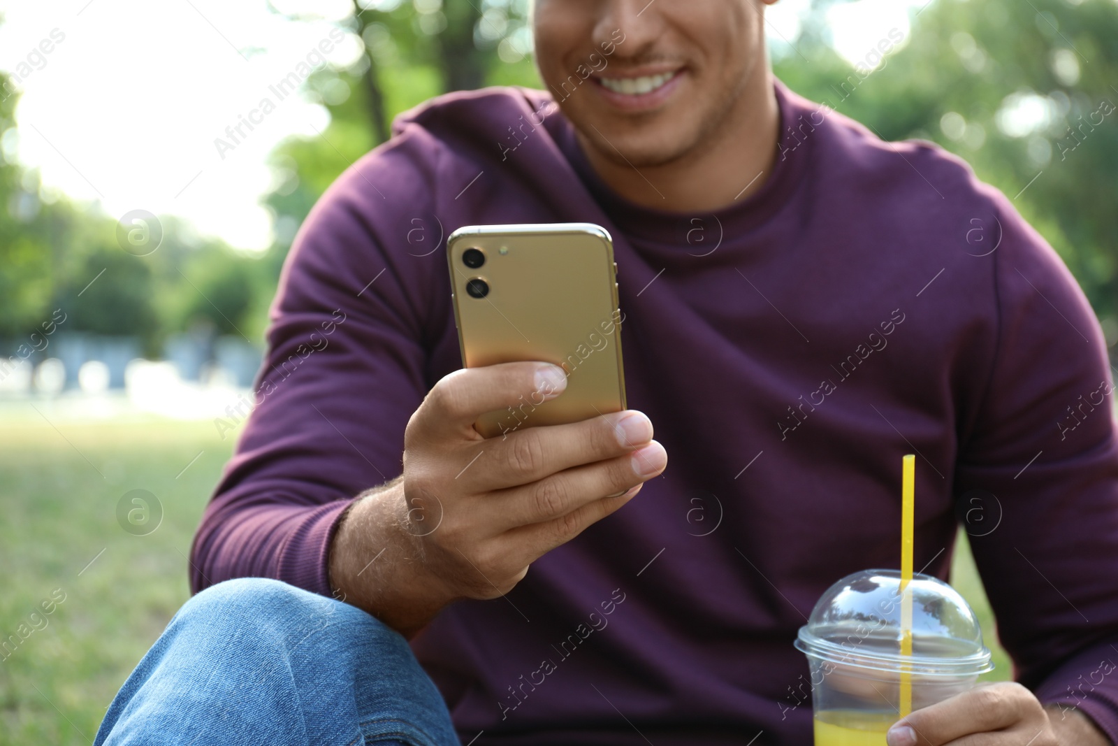 Photo of Man with smartphone and refreshing drink in park, closeup