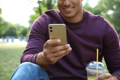 Man with smartphone and refreshing drink in park, closeup